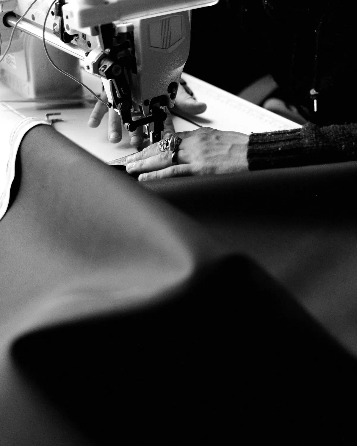 Hands feeding heavy black fabric through an industrial sewing machine.
