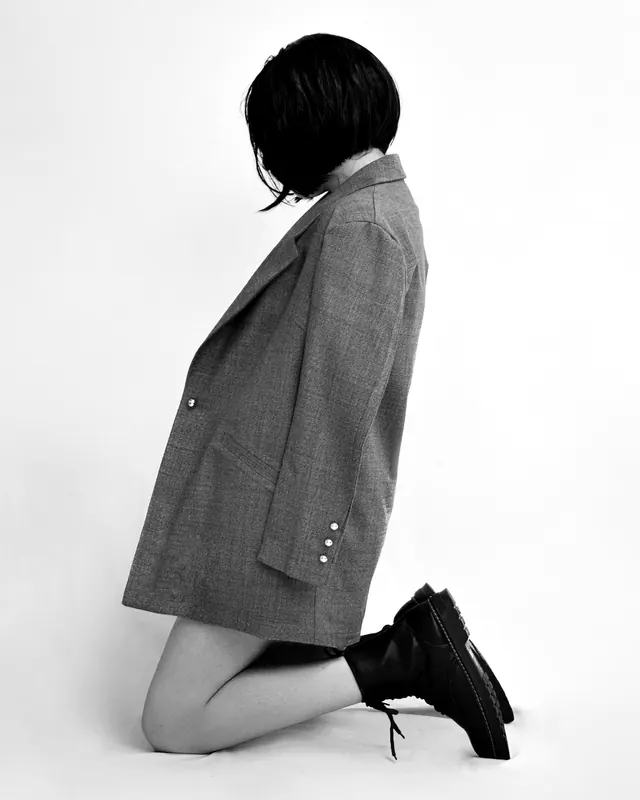 A model kneeling side-on in an oversized grey houndstooth blazer and black boots.