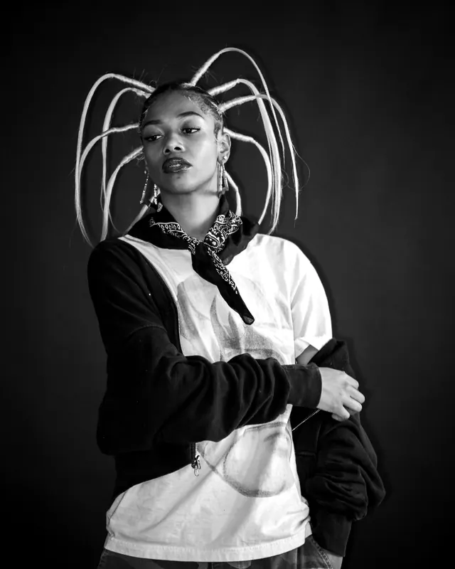 A model in a patched black and white hoodie with a bent wire halo rising from the hood.