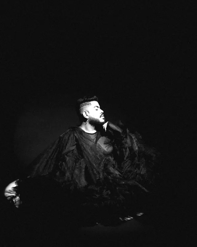 A man in a dark room wrapped in a voluminous cloak of black tulle.