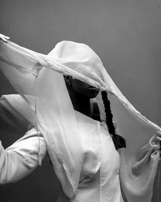 A figure in a white shirt lifting a sheer veil that is sewn into the collar.